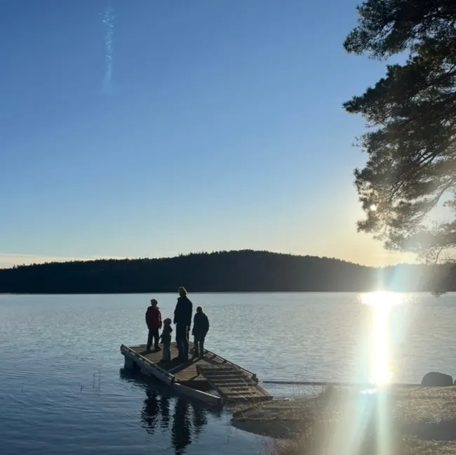 Fyra personer på en badbrygga vid vattnet i motljus.
