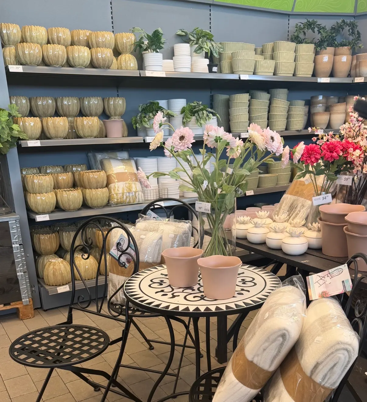 Butikshyllor med keramikkrukor, blommor och inredning.